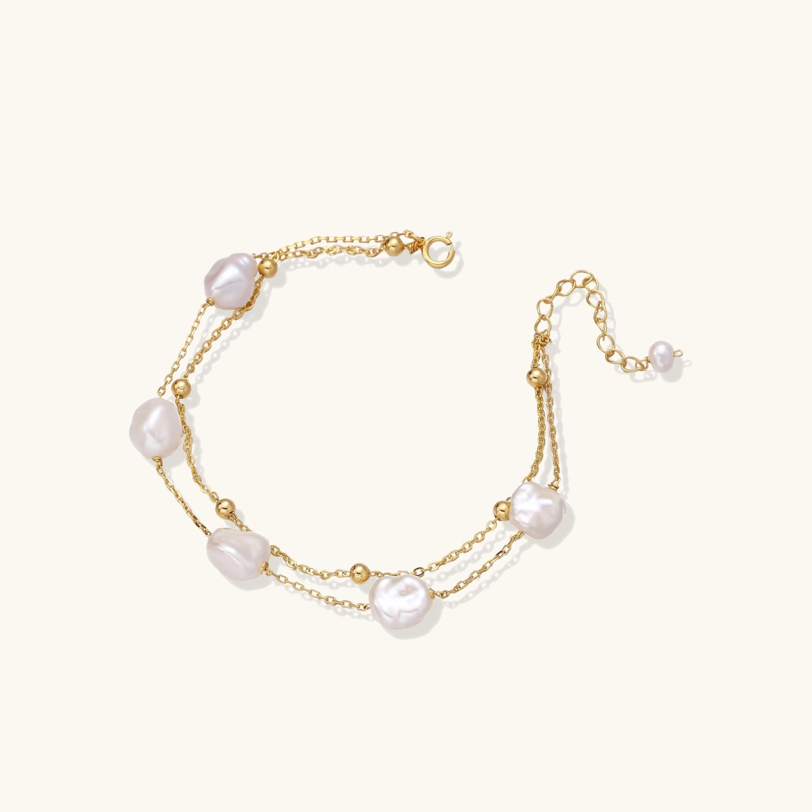 Double-strand gold bracelet with irregular baroque pearls and smooth freshwater pearls on cream background.