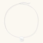 Minimalist brushed sterling silver dome pendant on delicate chain against cream background, showing matte textured finish